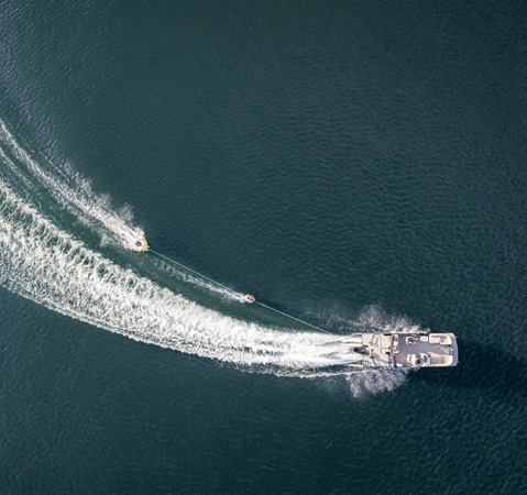 A Godfrey pontoon boat with a lounge layout pulling a water skier. 