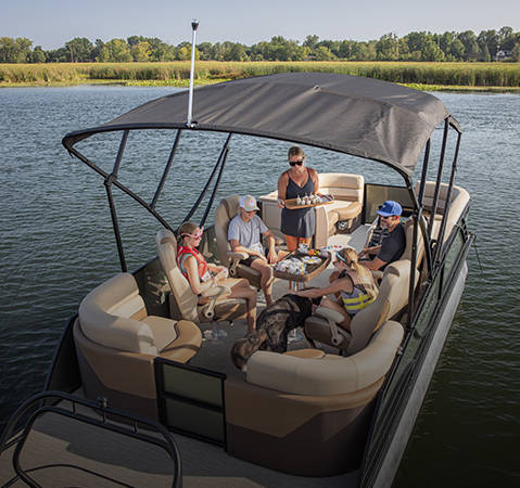A group of people enjoying a snack at the midship table on a Godfrey pontoon boat with a Quad Social (QS) layout.