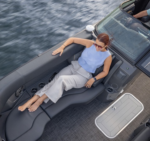 A woman relaxing on the bow split bench seat of a Godfrey pontoon boat with Split Bench layout.