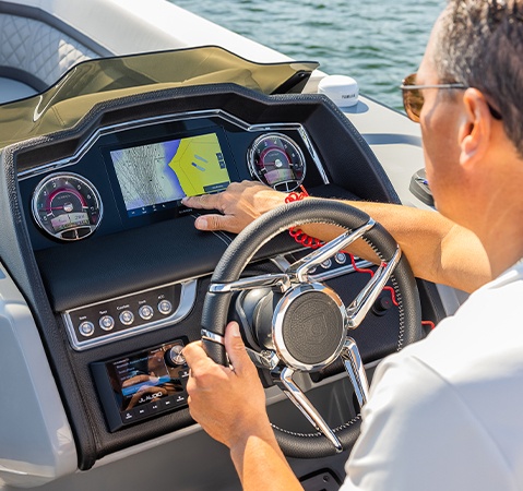 The helm of a Godfrey AquaPatio pontoon boat featuring a 7-inch multifunction display, tilt steering digital gauges, and RGB lighting control.