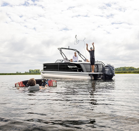 A man throwing a tow rope out to a wake boarder from his Godfrey AquaPatio pontoon boat.