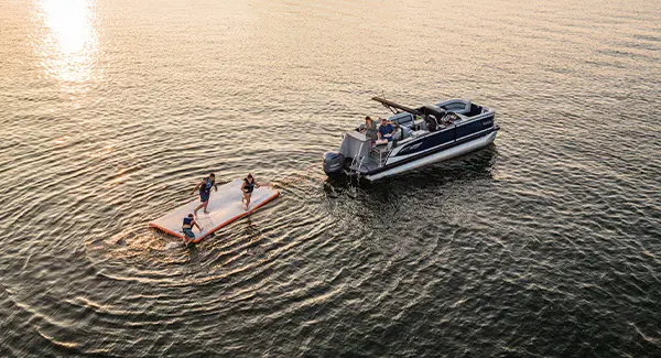 Aerial view of kids jumping off a float hooked to a Godfrey AquaPatio pontoon boat on a lake.
