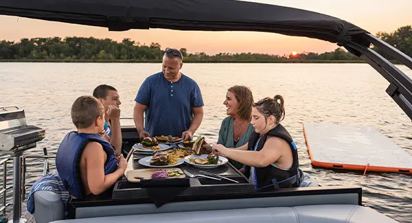 5 people enjoying a meal at the stern table on a Godfrey AquaPatio pontoon boat.