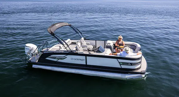 2 people relaxing on the split bench bow seating of a Godfrey AquaPatio pontoon boat.