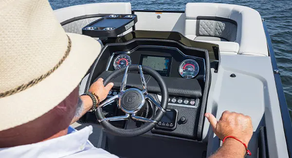 Over-the-shoulder view of a man at the helm and steering a Godfrey AquaPatio pontoon boat.