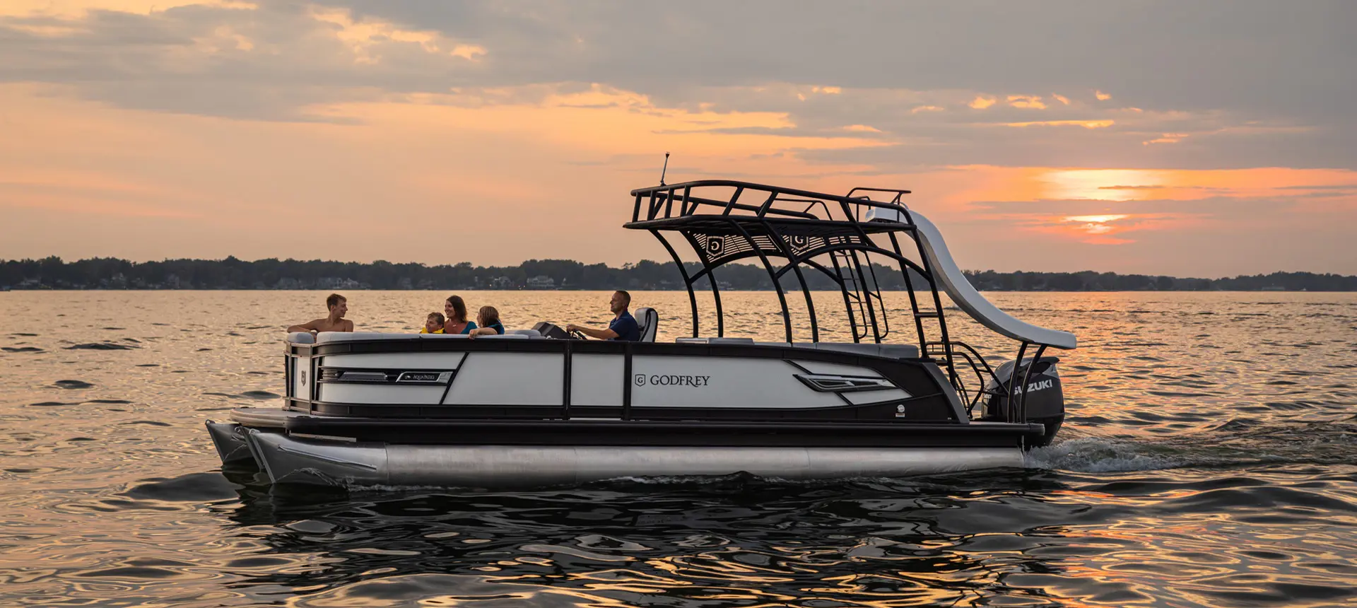 Side profile of a family of 5 floating the lake at sunset on a Godfrey AquaPatio pontoon boat.