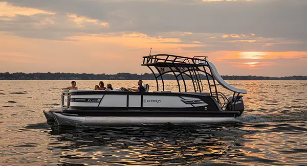 Side profile of a family of 5 floating the lake at sunset on a Godfrey AquaPatio pontoon boat.