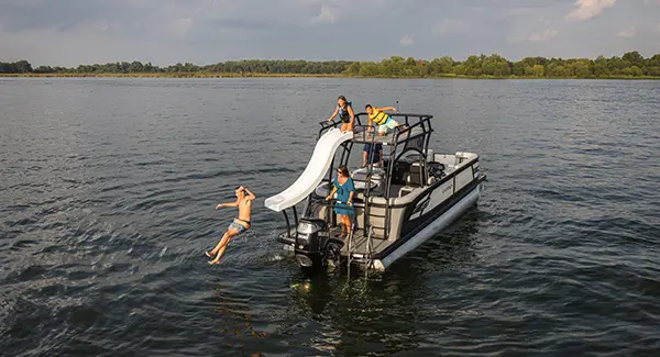 Kids sliding into the water from the top of a Godfrey AquaPatio pontoon boat.