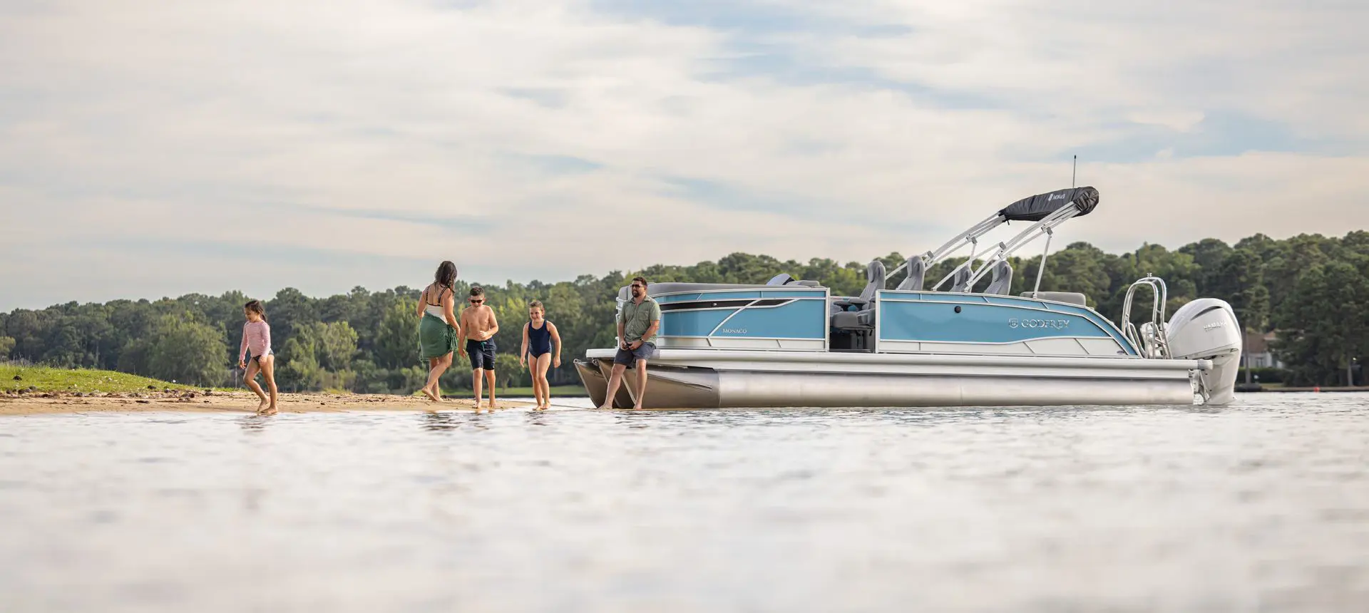 5 people on shore near a Godfrey Monaco pontoon boat.