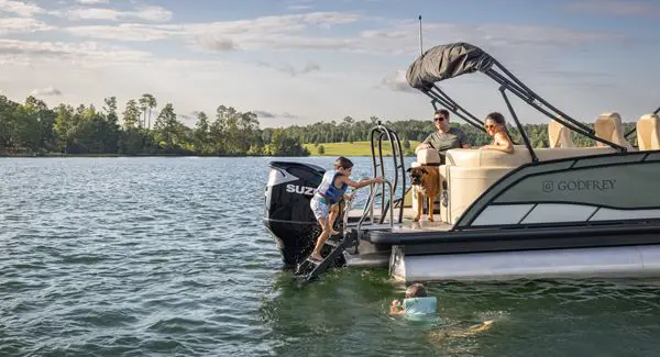 A kid climbing up the stern ladder on a Godfrey Monaco pontoon boat.