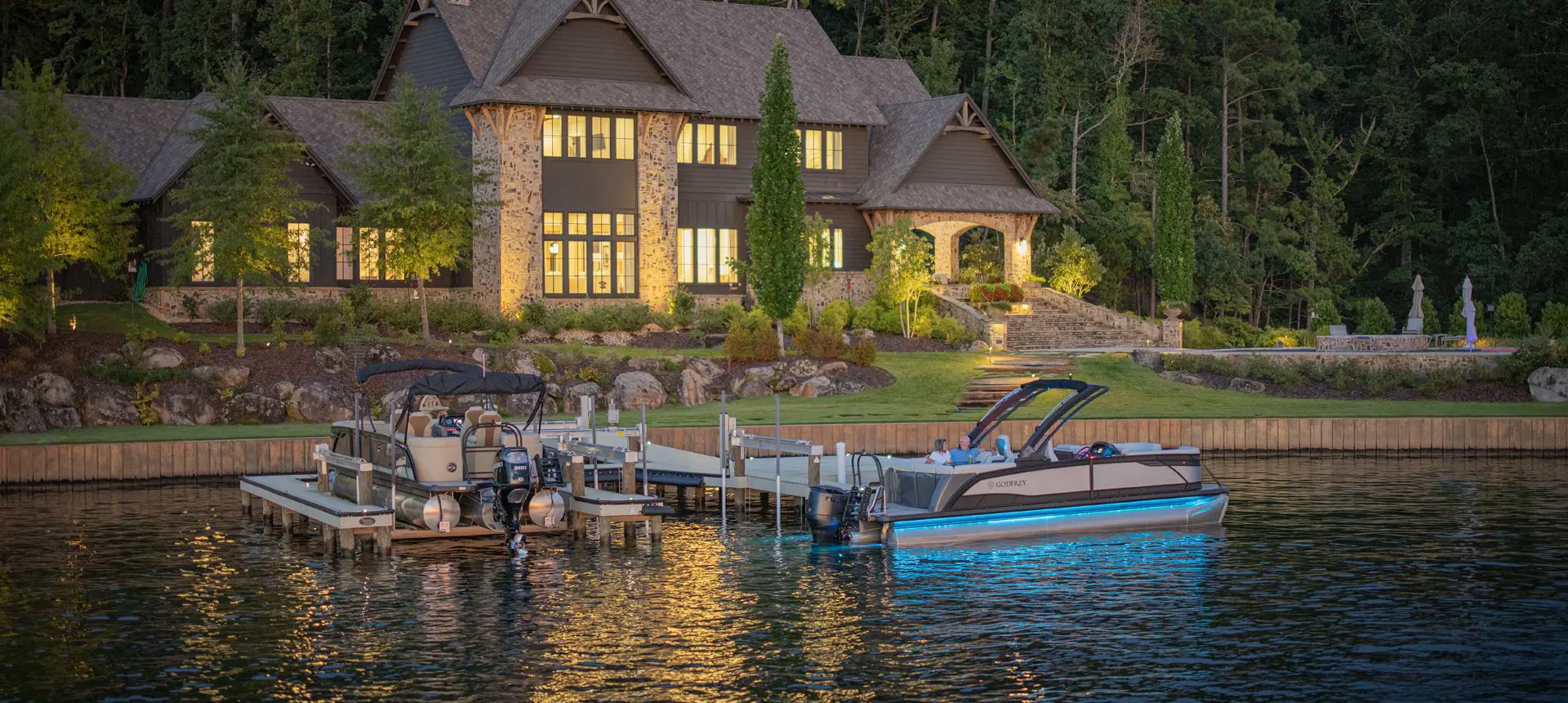 A Godfrey Monaco pontoon boat with RGB full-spectrum lighting docked near shore.
