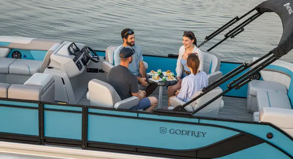 4 people enjoying a snack at the mid-ship table on a Godfrey Sweetwater pontoon boat.