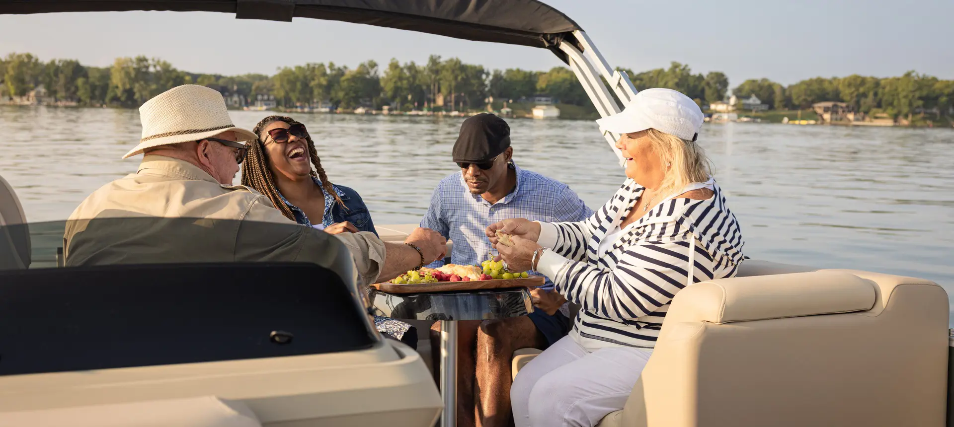4 friends enjoying a snack at the stern table on a Godfrey Sweetwater pontoon boat.