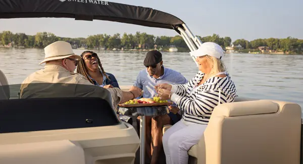 4 friends enjoying a snack at the stern table on a Godfrey Sweetwater pontoon boat.