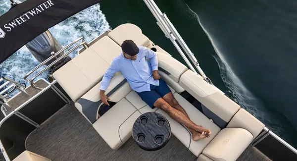 A man relaxing on the stern bench seating on a Godfrey Sweetwater pontoon boat.
