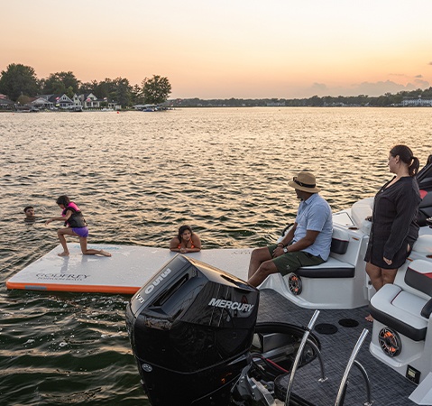 A man sitting at the stern jump seats on a Godfrey XP tritoon boat and watching his kids play in the water.