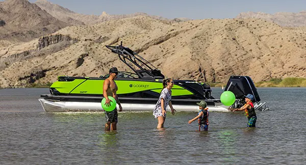 2 parents and 2 kids playing in the shallows near their Godfrey XP tritoon boat.
