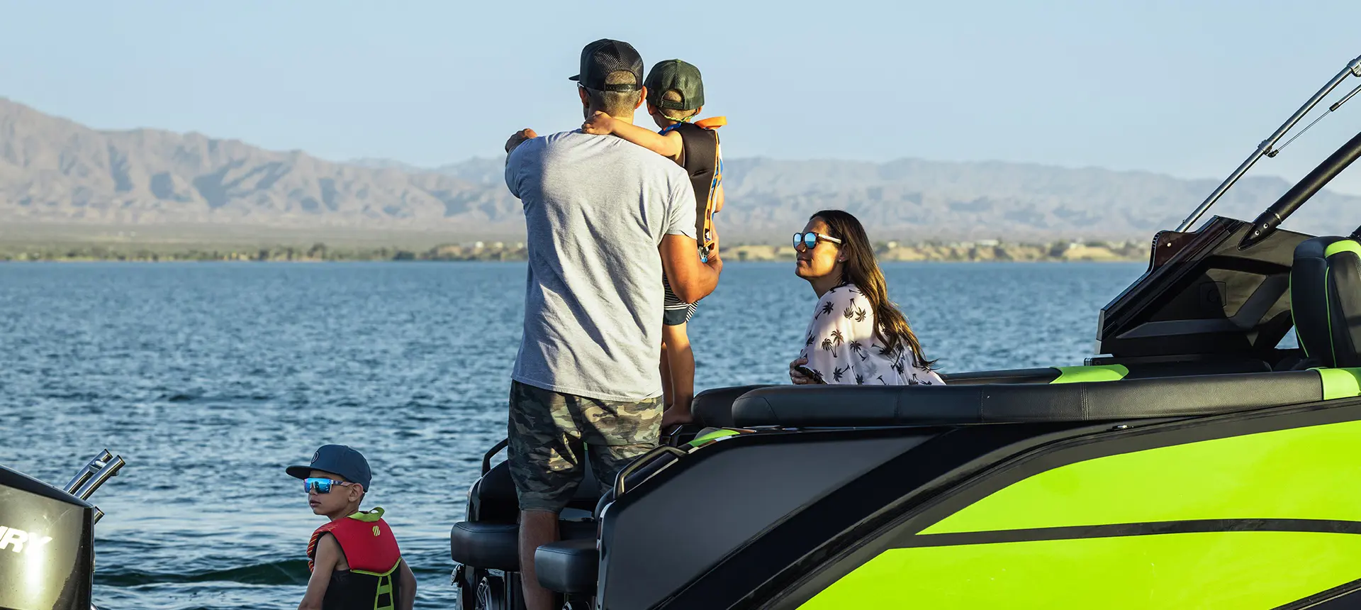 A father pointing to the horizon while holding his son on a Godfrey XP tritoon boat.