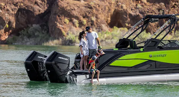 2 parents and 2 kids standing on the stern of a Godfrey XP tritoon boat.