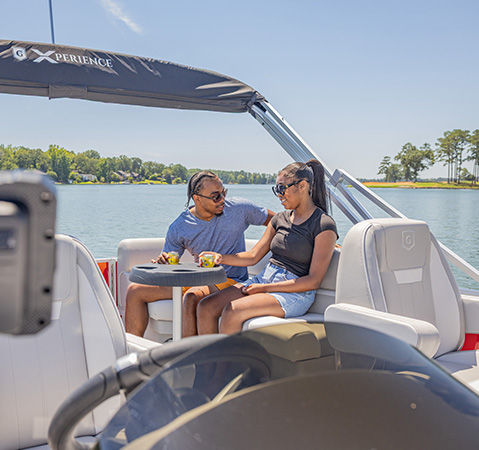 Woman grabbing a towel from the storage on the site of the split bench seating on a Godfrey Xperience pontoon boat.
