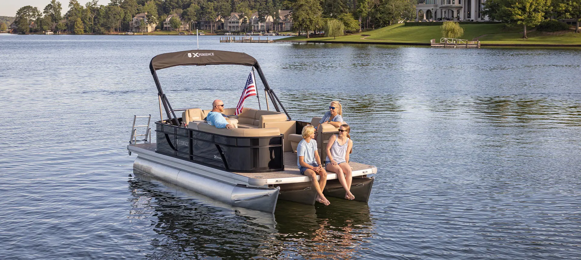 A family of four relaxing on a Godfrey Xperience tritoon boat while floating the lake.