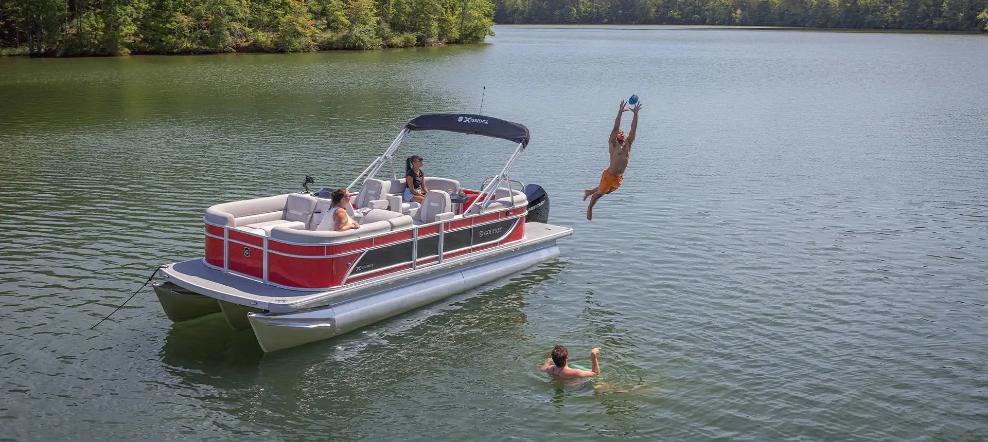 A guy jumping off the stern of a Godfrey Xperience pontoon boat to catch a football.
