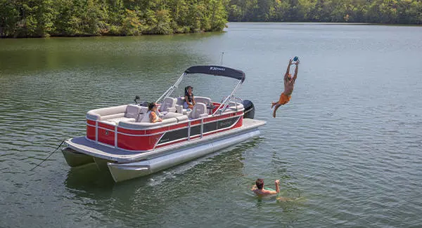 A guy jumping off the stern of a Godfrey Xperience pontoon boat to catch a football.
