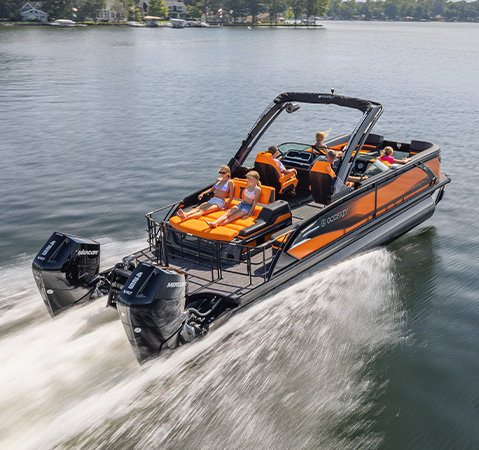 Godfrey AquaPatio pontoon boat with twin outboard engines carrying passengers across a calm lake.