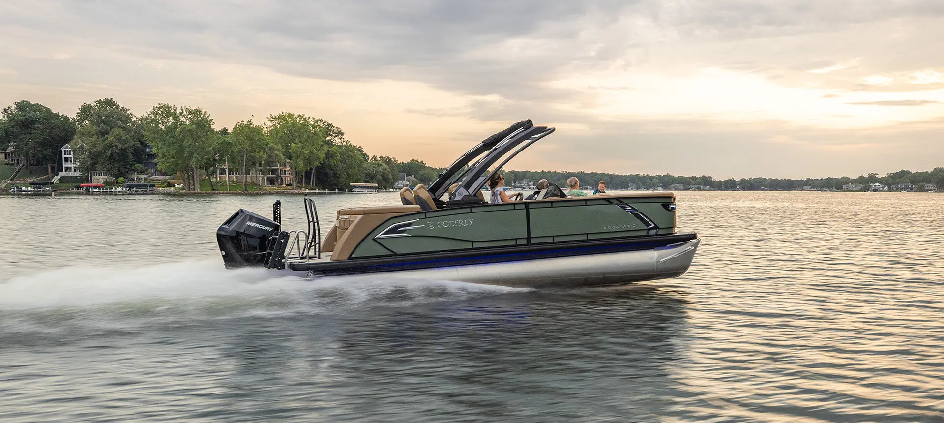 Side profile of a Godfrey AquaPatio pontoon boat cruising across a lake.