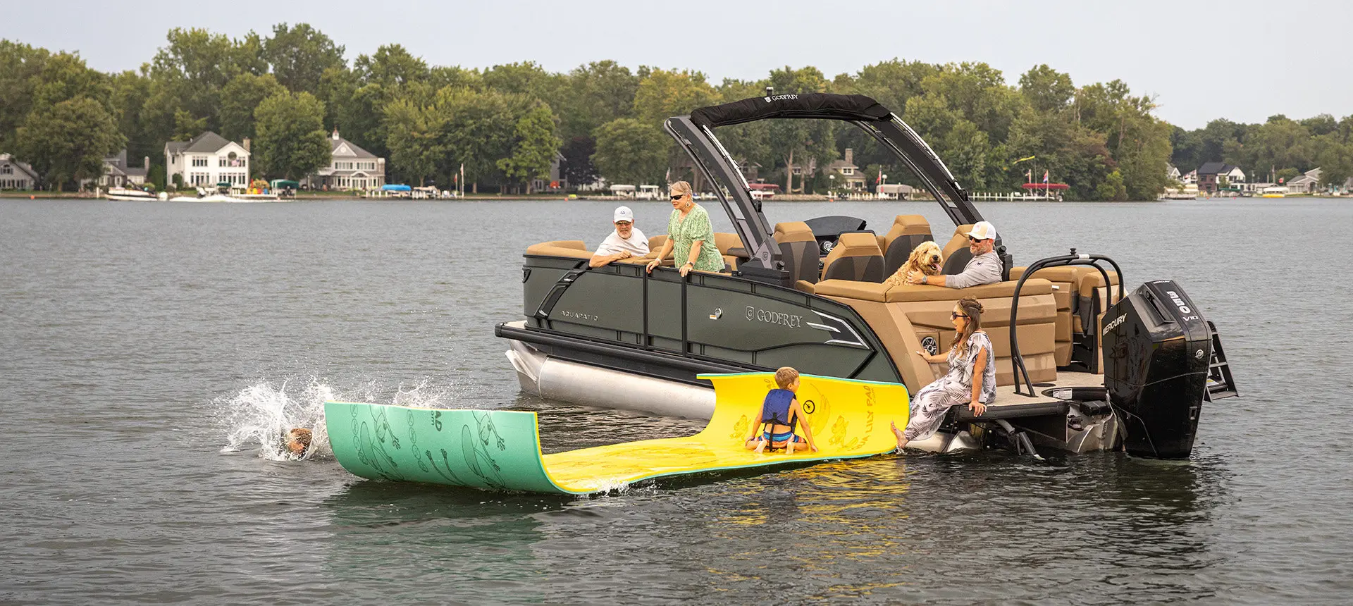 Kids jumping off a float hooked to a Godfrey AquaPatio pontoon boat on a lake.