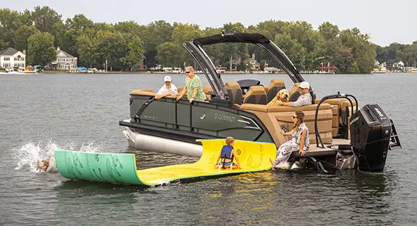 Kids jumping off a float hooked to a Godfrey AquaPatio pontoon boat on a lake.