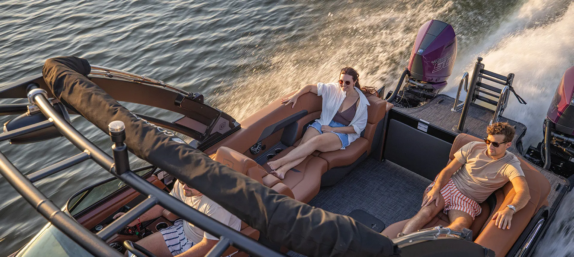 2 people relaxing on the stern split bench seats on a Godfrey AquaPatio tritoon boat with twin engines.