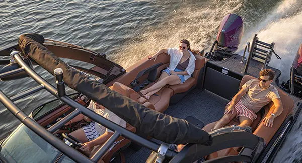 2 people relaxing on the stern split bench seats on a Godfrey AquaPatio tritoon boat with twin engines.