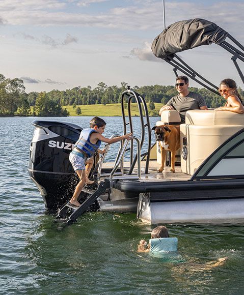 A child climbing up a ladder at the stern of a Godfrey Monaco pontoon boat