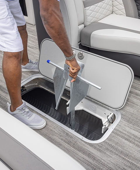 A person placing an anchor in an open storage compartment in the floor of a Godfrey Monaco pontoon boat