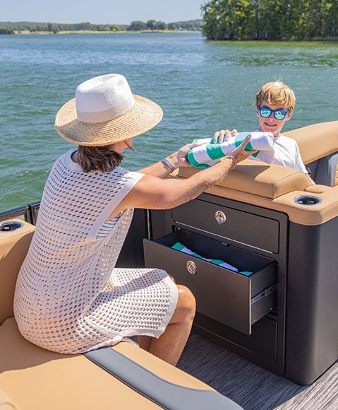 A woman holding a towel seated in front of an open drawer built into the chaise of a Godfrey Monaco pontoon boat