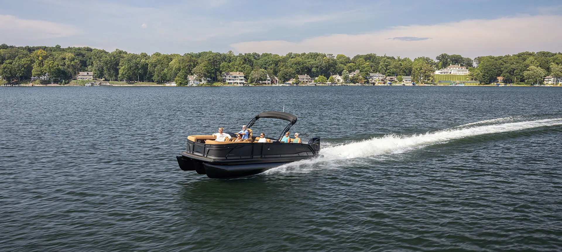 Far away view of a Godfrey Monaco pontoon boat cruising on a lake.