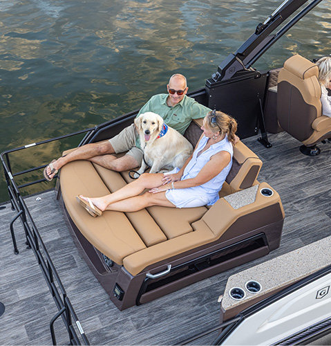 Two people and a dog sitting together on a lounger seat at the back of a Godfrey Sanpan pontoon boat