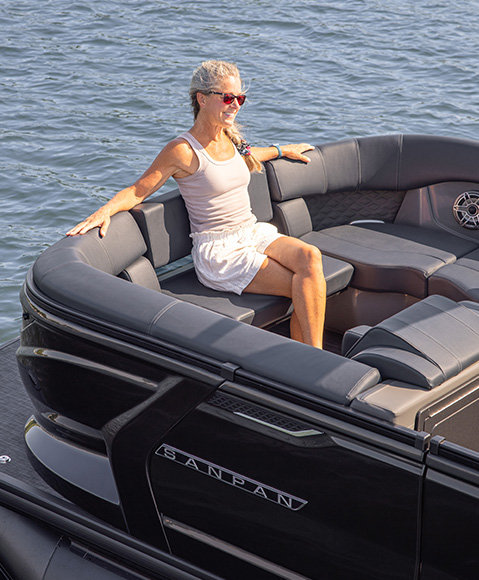 A woman sitting on a fold-out seat at the stern of a Godfrey Sanpan pontoon boat