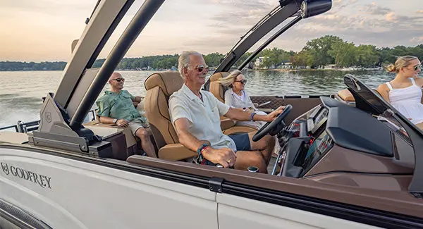 A man smiling while sitting at the helm and cruising the lake on his Godfrey Sanpan pontoon boat.