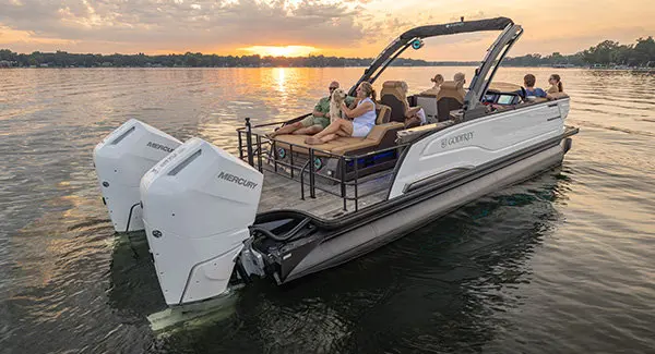 2 people sitting with their dog on the stern flip lounge seat on a Godfrey Sanpan pontoon boat at sunset.