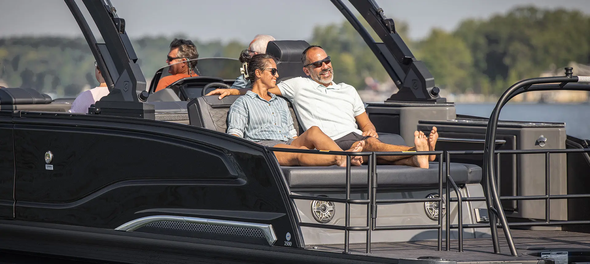 A couple smiling while relaxing on the flip lounge seat on the stern of a Godfrey Sanpan pontoon boat.