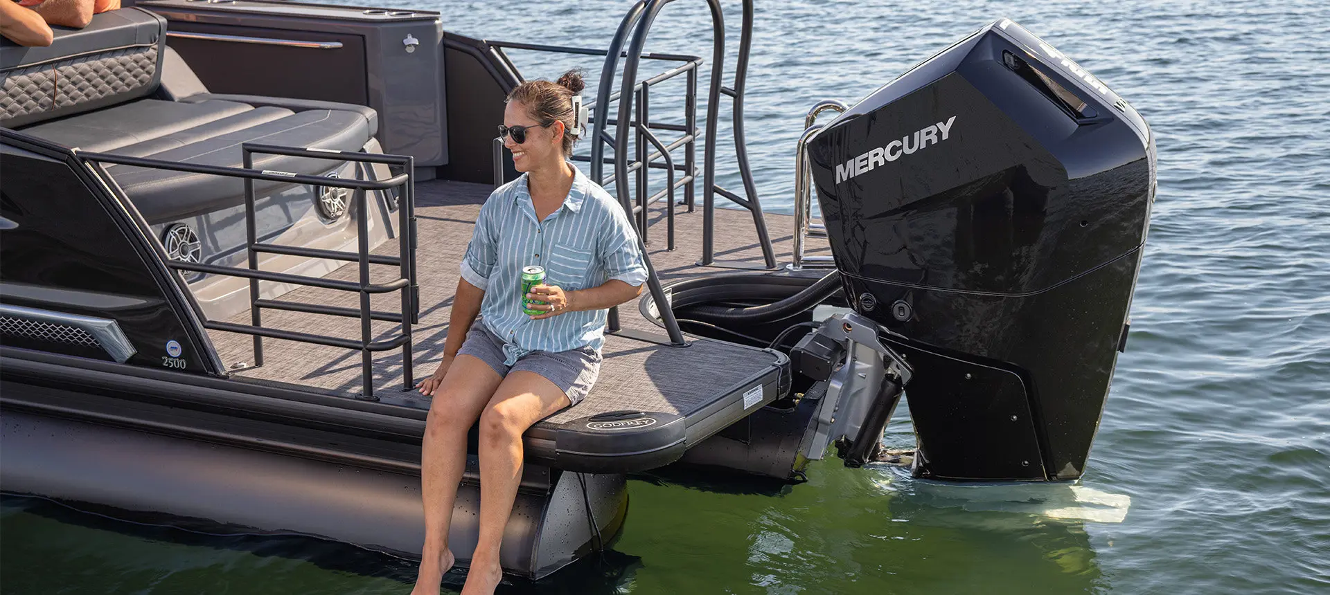 A woman sitting on the stern deck of a Godfrey Sanpan pontoon boat with her feet dangling toward the water.