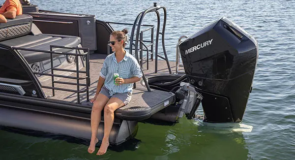 A woman sitting on the stern deck of a Godfrey Sanpan pontoon boat with her feet dangling toward the water.