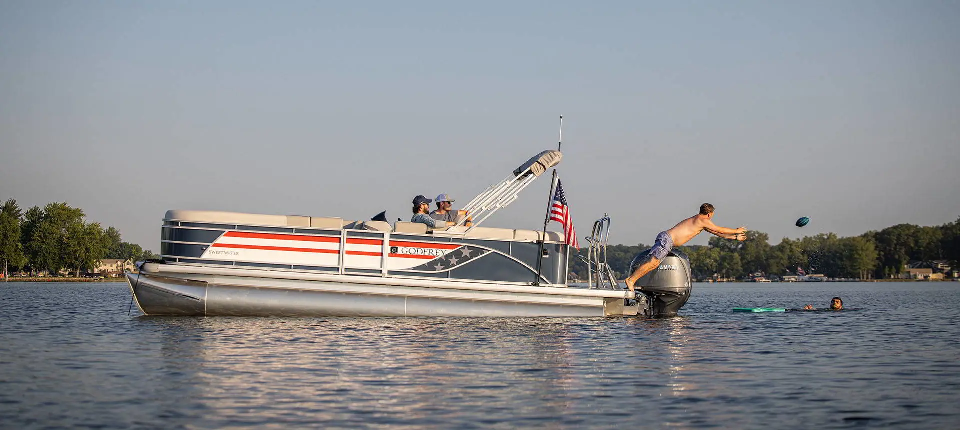 A kid jumping off the stern deck of a Godfrey AquaPatio pontoon boat to catch a football.