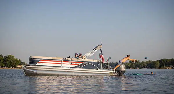 A kid jumping off the stern deck of a Godfrey AquaPatio pontoon boat to catch a football.
