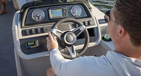 Over the shoulder view of a man sitting at at the helm of a Godfrey AquaPatio pontoon boat.