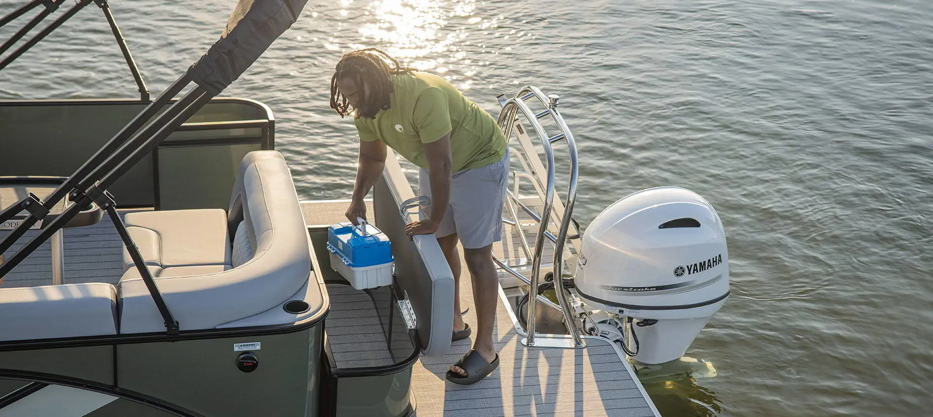 Man grabbing a tackle box from the in-seat storage of a Godfrey AquaPatio pontoon boat.