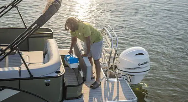 Man grabbing a tackle box from the in-seat storage of a Godfrey AquaPatio pontoon boat.