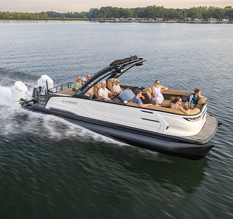 White Godfrey Sanpan luxury pontoon boat with twin outboard engines carrying passengers and a dog across the water.